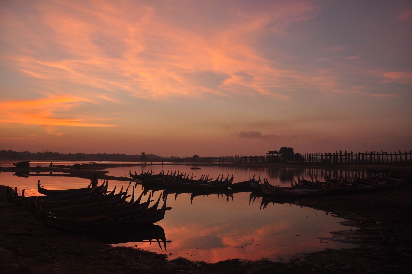 Boats silhouetted at dusk near the U Bein Bridge in Amarapura, Myanmar
